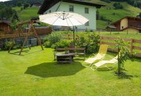 Gemütlicher Garten mit Liegen, Schwinge und Sonnenschirm im Raurisertal, umgeben von Natur.