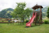 Spielplatz mit Rutsche und Tisch im Garten, umgeben von Bergen im Raurisertal.