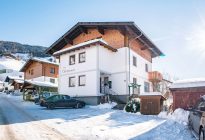 Haus Obersamer im winterlichen Raurisertal mit Bergblick und Autos vor dem Gebäude.